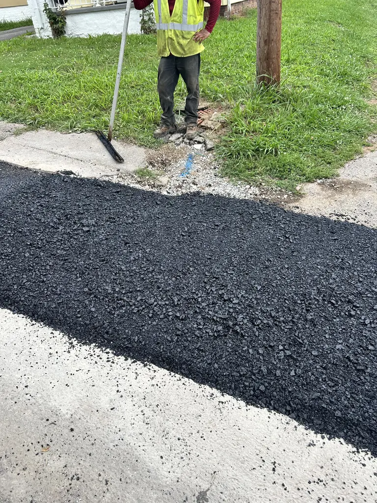 Crew member raking out new asphalt along a driveway edge in Knoxville, Tennessee